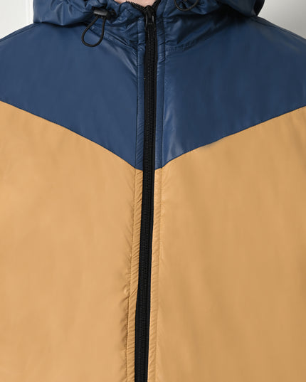 A man wearing a color-blocked windblock jacket with fleece inside mustard yellow and navy blue, with a hood