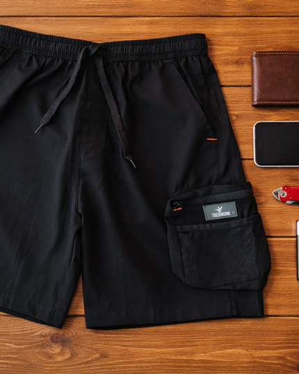 Black shorts with a phone, wallet, knife, and lighter on a wooden surface